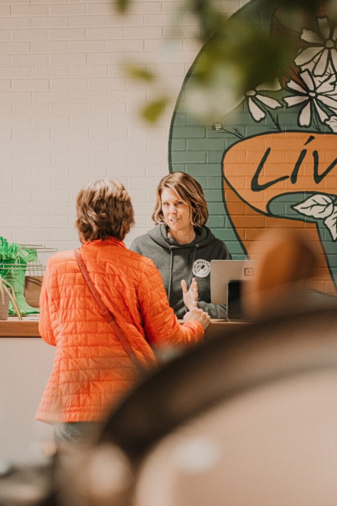 Woman conversing with shop attendant in a lively market environment.