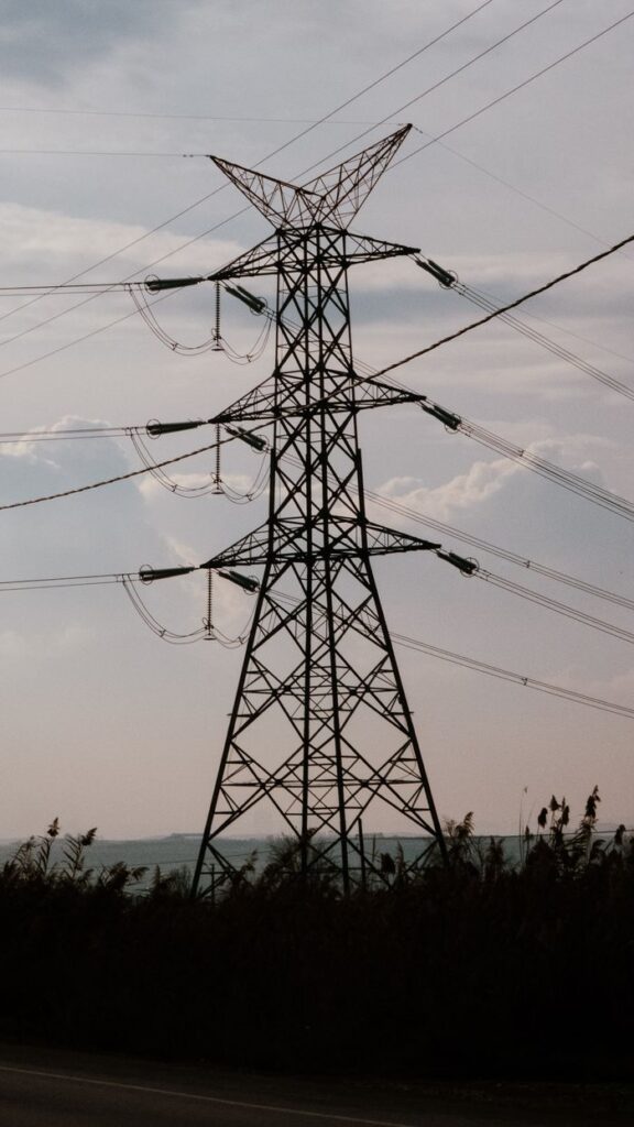 Silhouette of a high voltage power transmission tower against a cloudy sky.