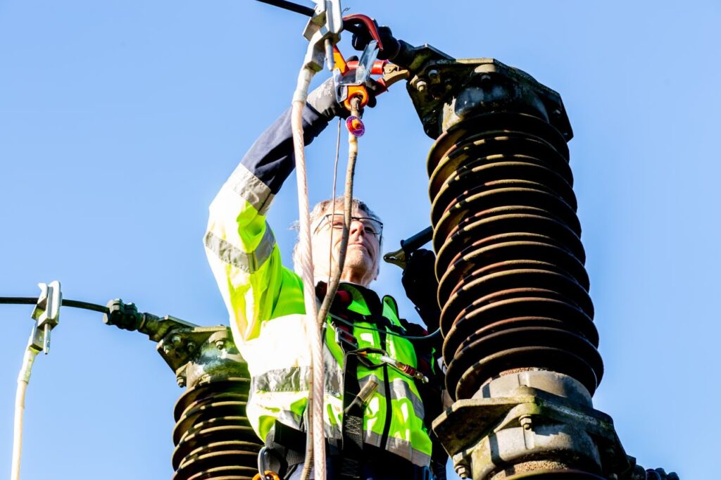Safety-conscious worker inspecting high-voltage power structures on a clear day.