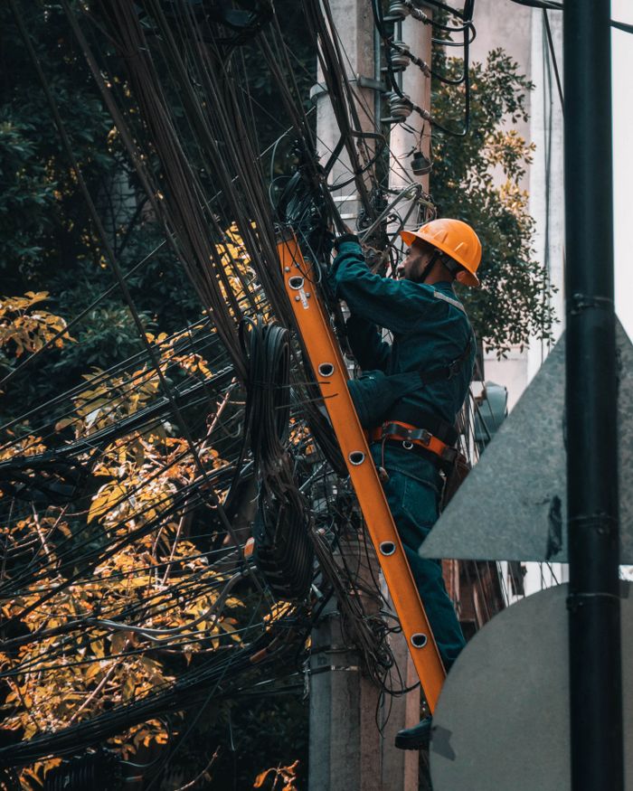 An electrician on a ladder fixing tangled power lines in Mexico City outdoors.